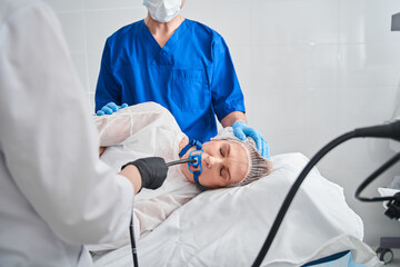 Woman laying at the bed while assistant holding special equipment at her mouth