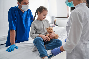 Two male and female pediatrician examining little girl child