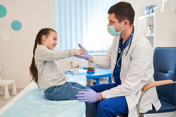 Happy little preschool girl giving high five to male doctor at meeting in hospital