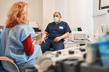 Calm man wearing protective mask and female patient talking at the hospital