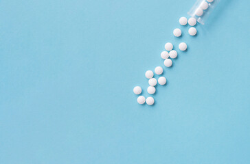 Different white pills and a plastic container on a blue background. Medical theme.	