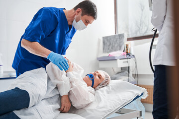 Doctor talking with his patient woman laying at the hospital bed before the colonoscopy