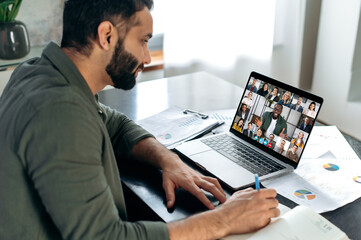 Successful indian man using a laptop, conducts virtual meeting with business partners on a video call. Group of diverse multiracial business people on laptop screen talking by video conference