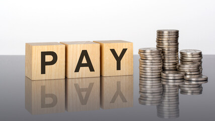pay - text on wooden cubes on a cold grey light background with stacks coins