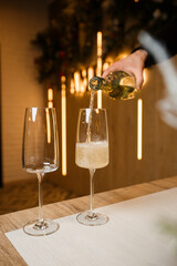Dispensing golden white wine into two wineglasses in a close up on the neck of the bottle over wood with copy space in a tilted angle view
