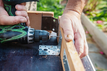 Close-up. A carpenter with his hands protected by gloves drills a wooden board with an electric...