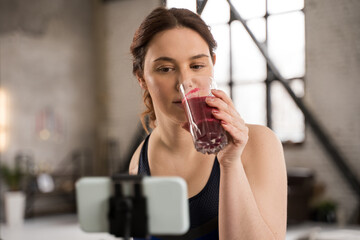 Female blogger without arm drinking smoothie while recording video blog at the smartphone