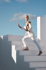 Unusual I take that as a compliment. Shot of a young model wearing stylish white clothes while walking up stairs against a sky background.