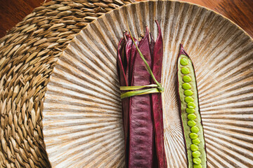 Bundle of purple Guaje bean pods on a plate next to an open bean pod with exposed seeds. Oaxaca,...