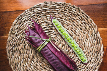 Bundle of purple Guaje bean pods on a plate next to an open bean pod with exposed seeds. Oaxaca, Mexico.