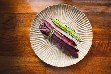 Bundle of purple Guaje bean pods on a plate next to an open bean pod with exposed seeds. Oaxaca,...