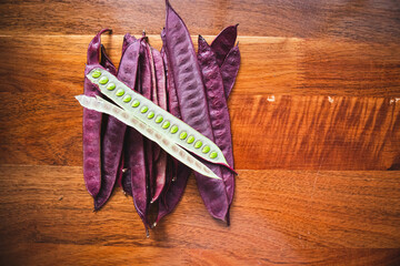 Pile of purple Guaje pod seeds on a wood table in Oaxaca Mexico. There is an open pod with seeds inside.