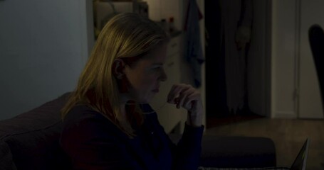 Woman sitting on couch with laptop looking up to a ghost lurking in the background