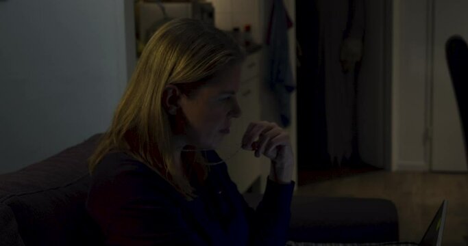 Woman sitting on couch with laptop looking up to a ghost lurking in the background