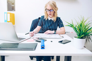 Beautiful business woman with glasses is sitting at an office desk looking at financial charts.