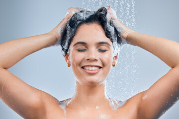 A warm shower keeps the stress away. Shot of a young woman washing her hair in the shower against a grey background.