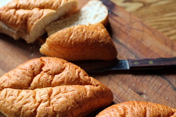 wheat bolillos made from wheat being sliced and ready to serve On a wooden cutting board at the kitchen table. Flat-lat photo.