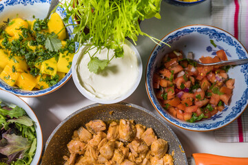 Sour cream, salsa, mango, cilantro, and fried salmon in bowls on a table, ingredients for fish tacos.