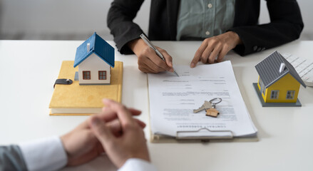 Fototapeta na wymiar Real estate agent assisting client to sign contract at desk with house model