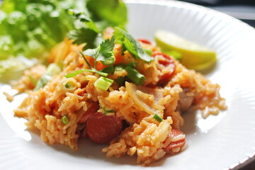 Close-up, pork and sausage fried rice served in a plate with lettuce and coriander garnish. Fried rice is a street food that is sold in Thailand.