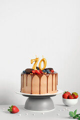 Chocolate birthday cake with berries, cookies and number seventy golden candles on White...