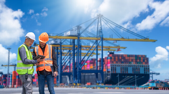 Engineer wearing uniform inspection and see detail on tablet with logistics container dock cargo yard with working crane bridge in shipyard with transport logistic import export background.