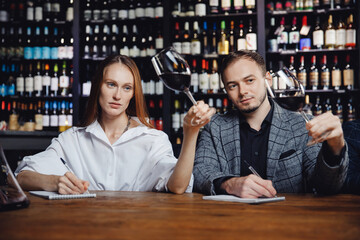 Professional sommeliers man and woman tasting red wine and taking notes at degustation notepad
