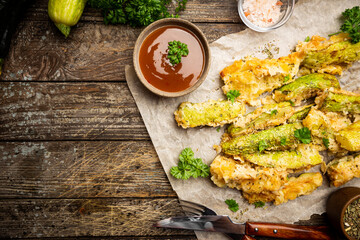 Zucchini sticks in batter, baked in oven over wooden background, top view