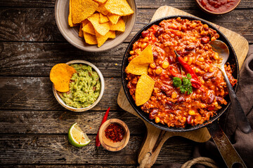 Mexican hot chili con carne in a pan with tortilla chips on dark background, top view