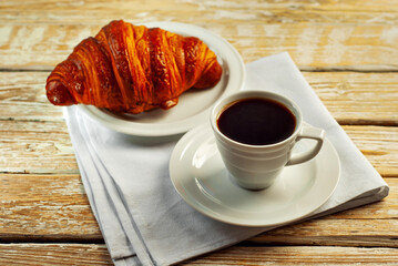 Coffee in a white ceramic mug. Croissant with coffee for breakfast. Coffee on an old wooden table.