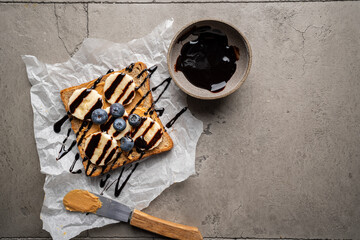 Peanut butter toast with banana slices and chocolate. Healthy breakfast or snack on grey concrete background., top view