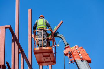 Male builders work at height in a lifting cradle, creating the iron frame of the building.