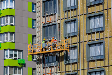 Male builders work on the facade of the building in a suspended cradle. Construction works.
