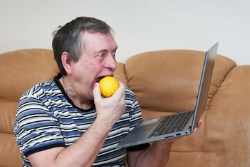 Freak eats lemon while holding a laptop while sitting on the couch - 499363128