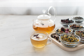 Glass cup with hot tea and a kettle on a bright table by the window Tray with different varieties of herbal tea on a white background Delicious and healthy drink Banner Space for text