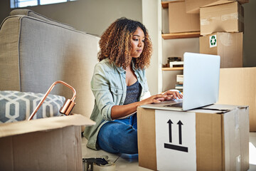 So much to do still. Shot of a focused young woman working on a laptop while seated on the floor and with boxes all around her at home.