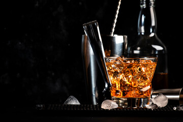 Godfather alcoholic cocktail with scotch whiskey, amaretto liqueur and ice. Black bar counter background, steel bar tools, copy space