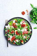 Delicious summer salad with sweet  figs, white feta cheese, walnuts, arugula and jam vinegar dressing on white table background, top view, negative space