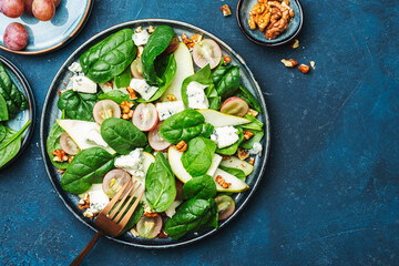 Delicious summer salad with pear, grapes, roquefort cheese, spinach, walnuts on blue table background, top view, negative space