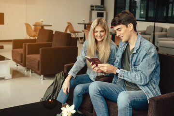 Young traveler lover couple holding and looking  passport and boarding pass while waiting airline flight to travel at airport terminal.