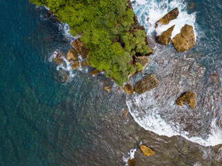 Coral Island which overgrown by trees on the beach and hit by the wave.the sea water looks clear and blue 