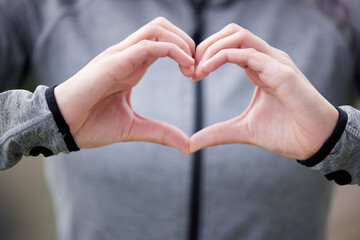 Health comes first, always. Shot of a woman forming a heart shape with her hands while out for a run.