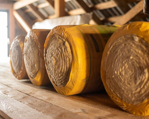 Insulation rolls in yellow packaging in the attic of a wooden house. r - obrazy, fototapety, plakaty