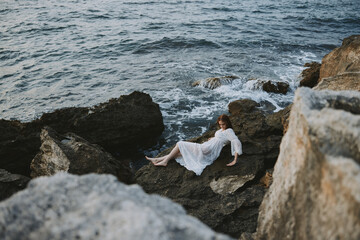 beautiful woman in a secluded spot on a wild rocky coast in a white dress unaltered