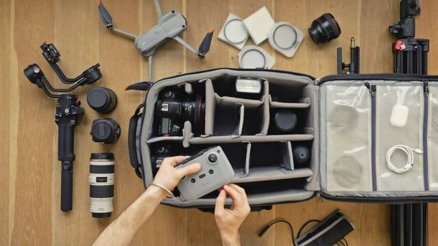 Professional  photographer packs smart backpack with equipment screw the stick into the remote controller. Top view on suitcase with lens camera and drone drone and gimbal