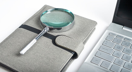 Magnifying glass at notebook with open laptop. Schedule, agenda analysis, planning. High quality photo