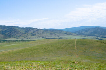 Road through green hills. There are blue mountains in the distance. Summer landscape.