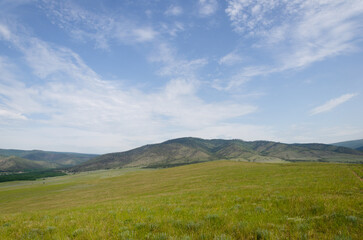 Naklejka premium Bright green meadows extend into the distance to the blue mountains. The sun is shining brightly.