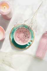 Pink tea in tea cup on white table with sunlight , candle, flower and glass bottle. Relaxing tea...