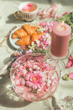 Aesthetic Breakfast With Glass Water Bowl And Pink Flowers With Candle, Croissants And Tea Cup. Elegant Food And Drink Concept. Fancy Drink With Flowers. Top View.